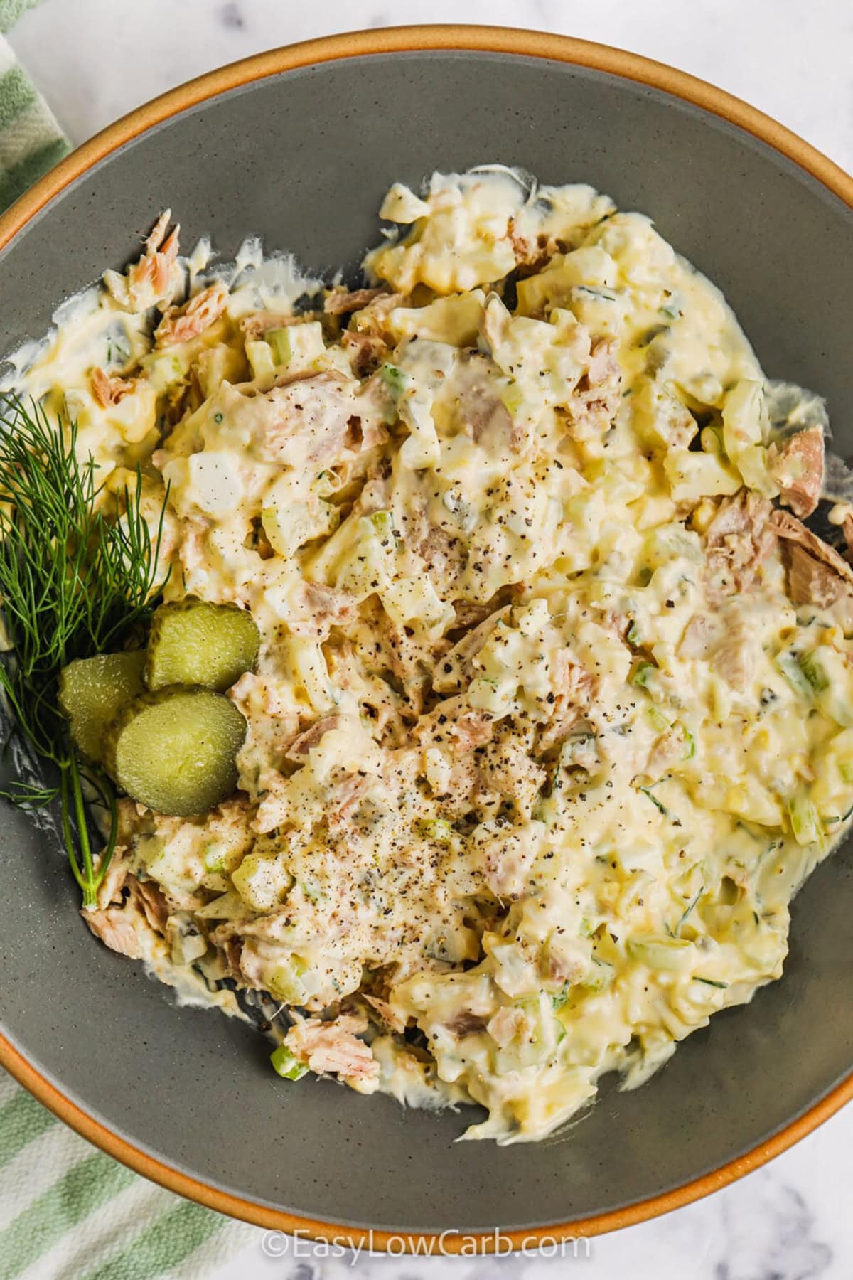 Tuna and egg salad is a simple, satisfying low-carb meal that’s perfect for busy days. Combining creamy mayo with boiled eggs, well-drained tuna, crunchy celery, and dill pickles creates a refreshing and flavorful salad. A touch of mustard and dill adds the perfect tang. It’s a versatile meal that’s great served in lettuce cups, wrapped in low-carb tortillas, or on a bed of fresh greens. #easylowcarb Tuna and Egg Salad with pickle slices on top