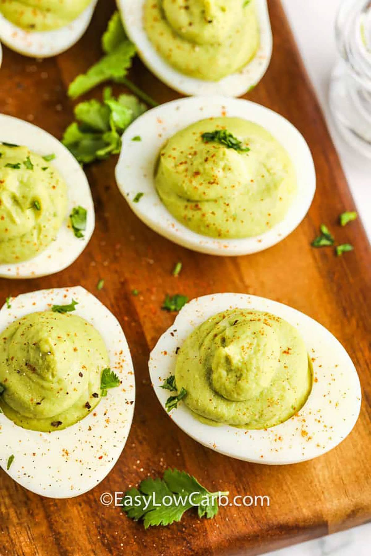 Avocado deviled eggs are a tasty, creamy, and nutritious twist on a party favorite! Mashed avocado adds richness and healthy fats, while a dash of lemon juice and garlic powder bring a bright, flavorful kick. They’re easy to make, naturally low-carb, and great for any occasion. Just fill, garnish, and serve up these irresistible bites. Perfect for a quick snack or a crowd-pleasing appetizer! #easylowcarb Avocado Deviled Eggs on a cutting board