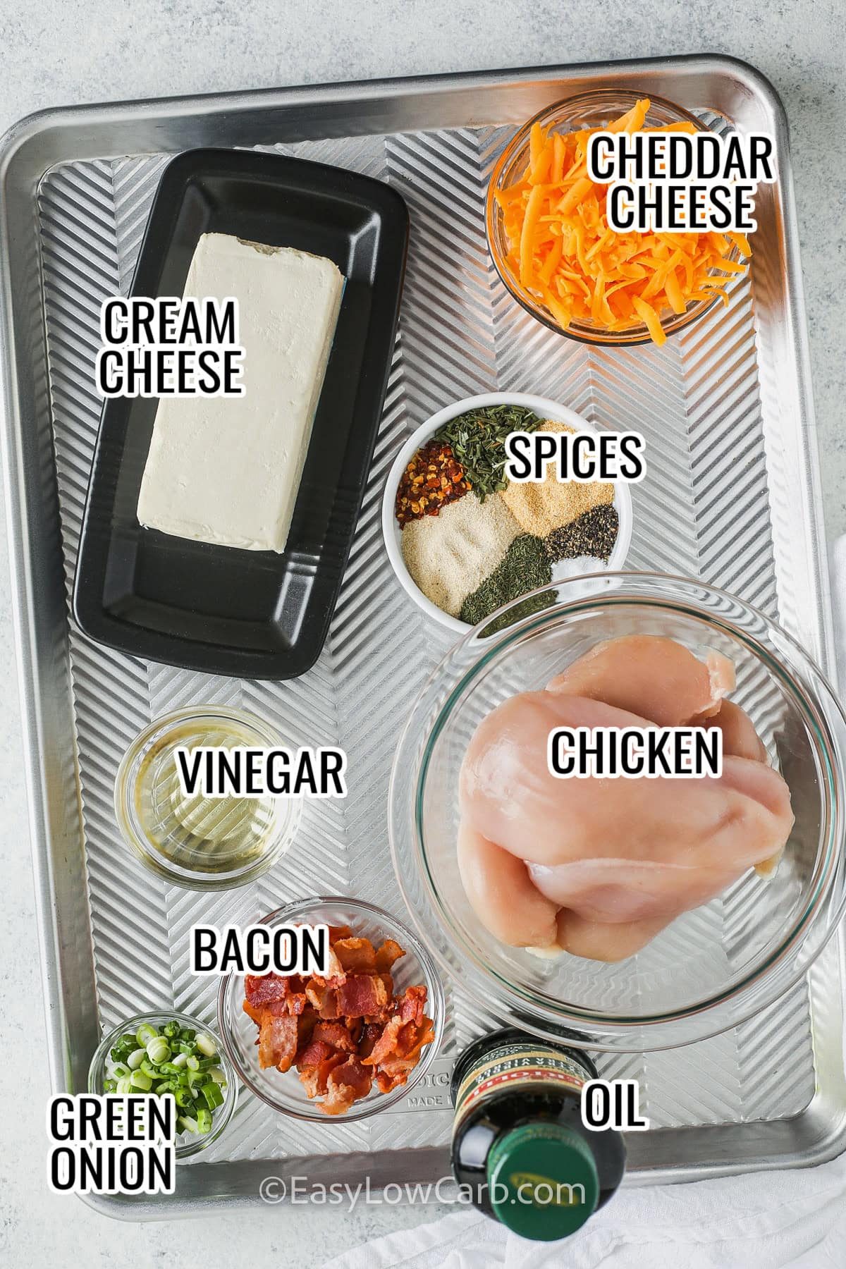 ingredients assembled to make crack chicken casserole, including cream cheese, cheddar cheese, spices, vinegar, chicken, bacon, green onions, and oil