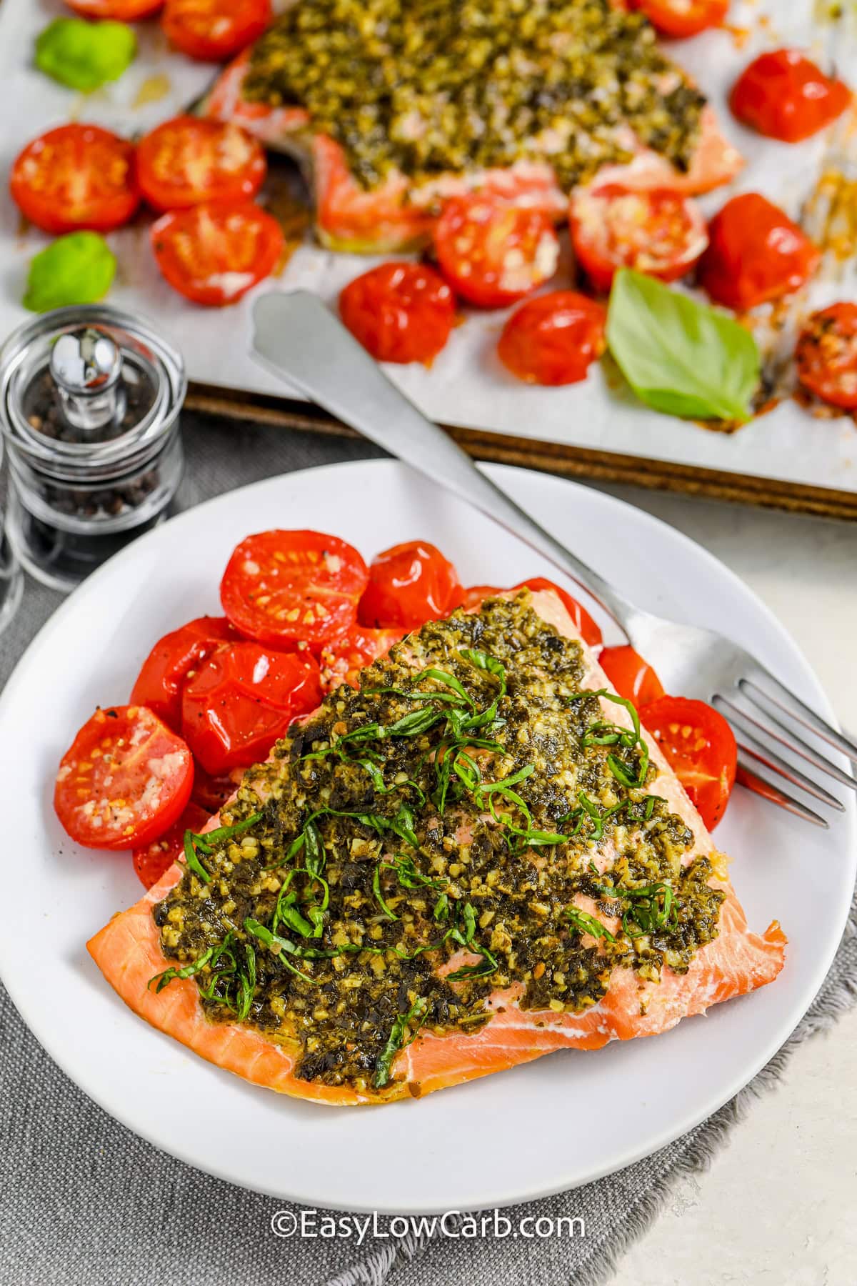 This pesto salmon recipe is a flavorful, low-carb meal made in one pan for easy cleanup! The salmon fillets cook perfectly with a pesto crust, while cherry tomatoes roast alongside, soaking up the garlicky olive oil. It’s a fast, healthy dinner ready in under 20 minutes. Serve with your favorite veggie or a light salad for a complete meal that’s satisfying without the carbs! #easylowcarb plated Pesto Salmon Recipe with sheet pan full