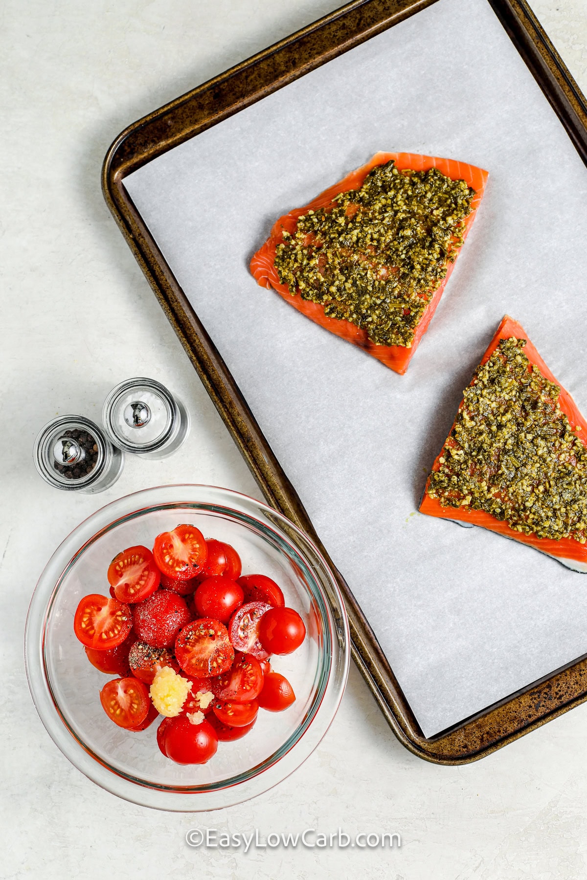 adding salmon with pesto to sheet pan with a bowl of tomatoes and seasonings to make Pesto Salmon Recipe