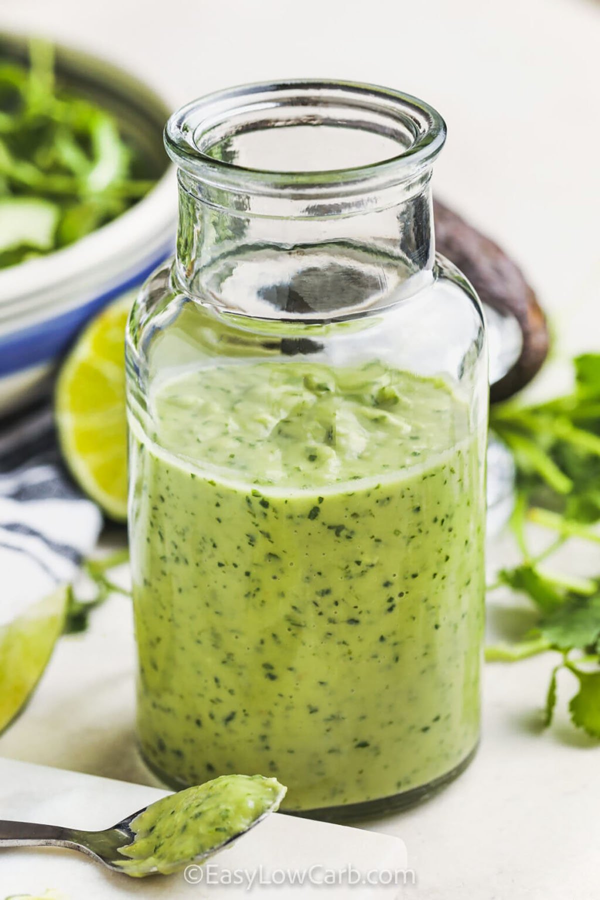 Avocado Lime Dressing in a jar and on a spoon with salad in a bowl
