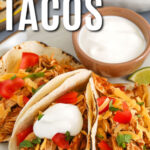 Chicken Tacos on a plate with cheese and sour cream with writing
