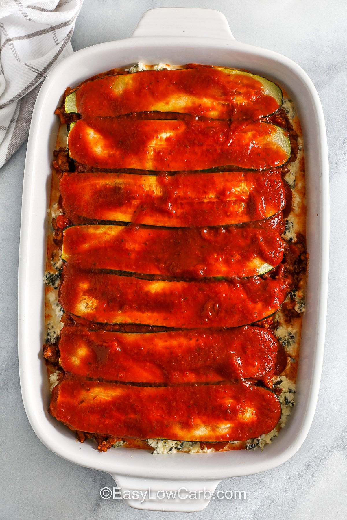 adding last layer of zucchini and pasta sauce to dish to make zucchini lasagna recipe