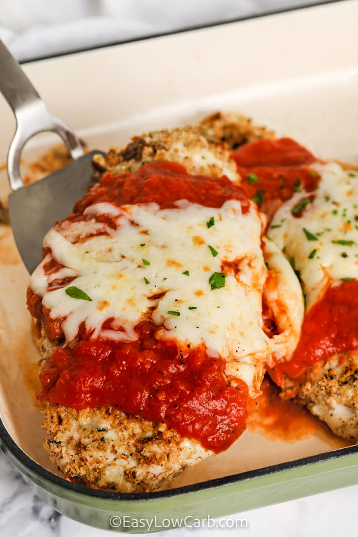 Oven baked chicken Parmesan is a low carb twist on the beloved Italian classic, featuring juicy chicken cutlets coated in crispy keto-friendly breadcrumbs and savory Parmesan cheese. Baked until golden and topped with rich, tangy pasta sauce and melty mozzarella, this dish delivers all the comfort food satisfaction without the carbs. Perfect for busy weeknights or a cozy family dinner. #easylowcarb Oven Baked Chicken Parmesan in the casserole dish