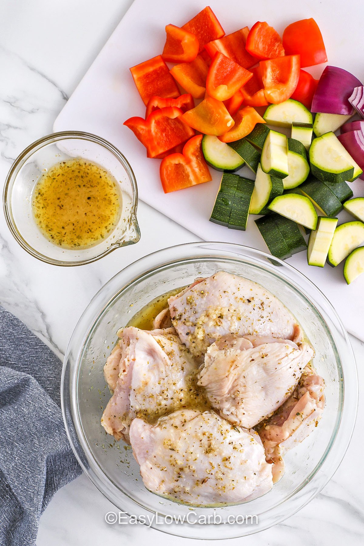 marinating chicken and chopped up vegetables to make Greek Sheet Pan Chicken