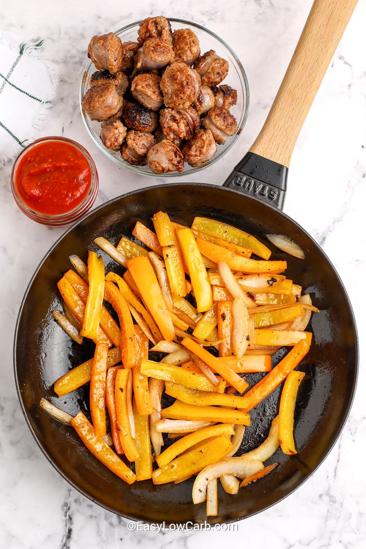 cooked peppers in a pan with a bowl of cooked italian sausage and a jar of tomato sauce to make Italian Sausage and Peppers