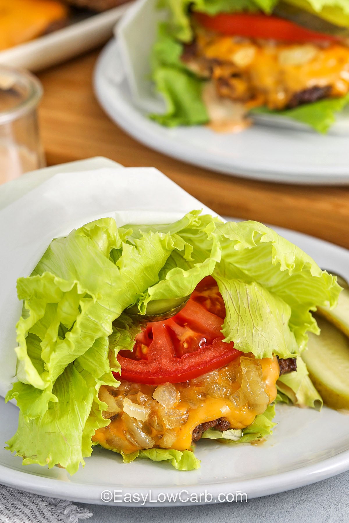 This lettuce wrap burger is loaded with a savory beef patty, melted cheese, creamy sauce, crisp pickles, tomato, and optional buttery onions. Wrapping the fillings in layered iceberg lettuce keeps every bite cool and crunchy while making the meal naturally low carb. Prepare the sauce and toppings before cooking so the burgers can go straight from the skillet to the table. Save this practical recipe for a quick dinner. #easylowcarb close up of toppings for Lettuce Wrapped Burger