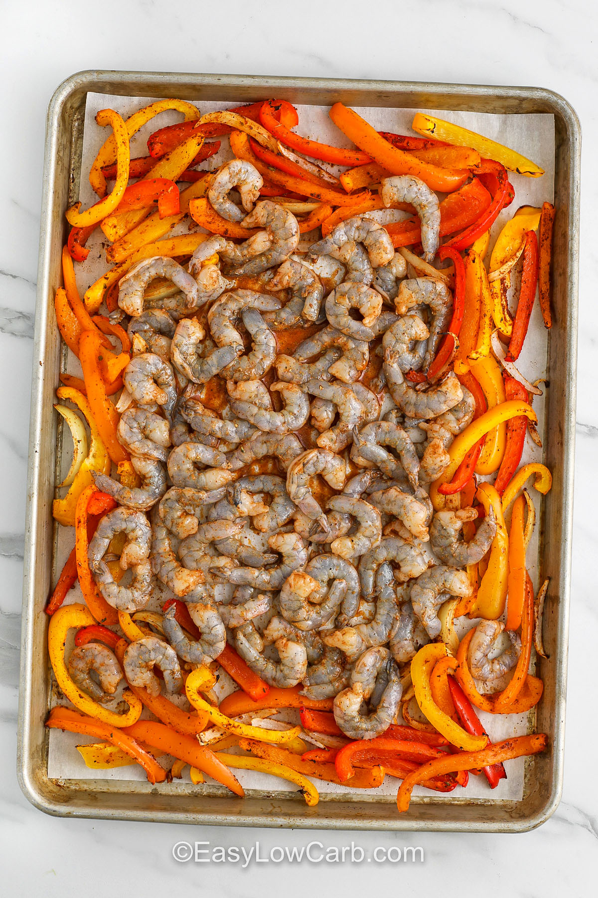 Sheet pan shrimp fajitas are a quick, low-carb recipe that delivers on flavor. Roasting bell peppers, onions, and shrimp in the oven with fajita seasoning brings out the natural sweetness of the veggies while infusing them with smoky, savory spices. This dish is super simple and can be served in low-carb tortillas, lettuce wraps, or with cauliflower rice. It’s a perfect meal prep idea for anyone cutting carbs without sacrificing taste! #easylowcarb adding shrimp to cooked veggies to make Sheet Pan Shrimp Fajitas