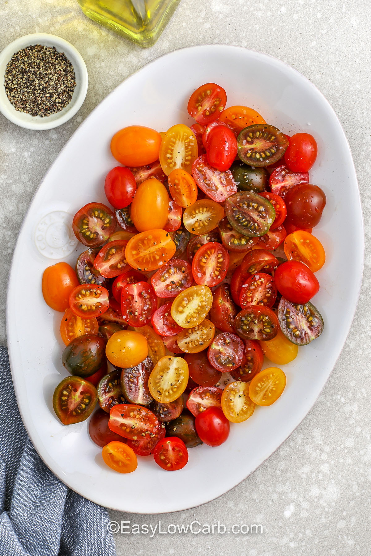 Tomato burrata salad is a beautiful dish that’s as impressive as it is easy. Just halve some cherry tomatoes, season, add burrata, and finish with basil and olive oil. Each bite delivers sweet, creamy, and herbaceous flavors. Balsamic glaze adds extra zing. It’s an effortless low-carb recipe you’ll reach for again and again. Perfect for picnics, brunches, or anytime snacking. #easylowcarb adding juicy tomatoes to plate to make Tomato Burrata Salad