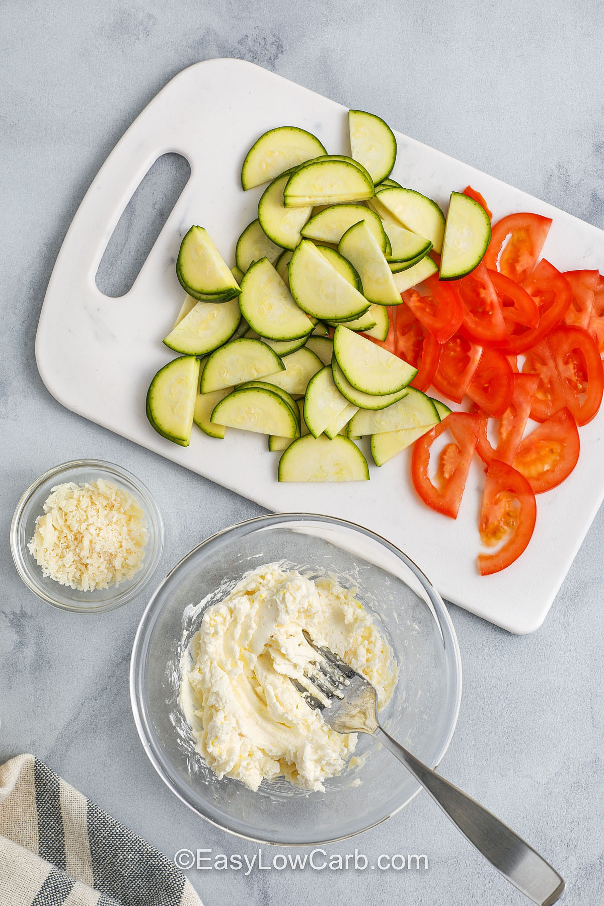 This Hasselback chicken recipe is an easy, flavorful, and low carb dinner idea that looks as good as it tastes. Juicy chicken breasts are sliced and stuffed with creamy cheese, zucchini, and tomato, then oven baked until golden and tender. It’s packed with protein and simple to make for any night of the week. Serve it as a hearty family meal or an elegant dish for a special holiday dinner. #easylowcarb tomatoes and zucchini sliced on a cutting board, with the cream cheese mixture prepared in a bowl