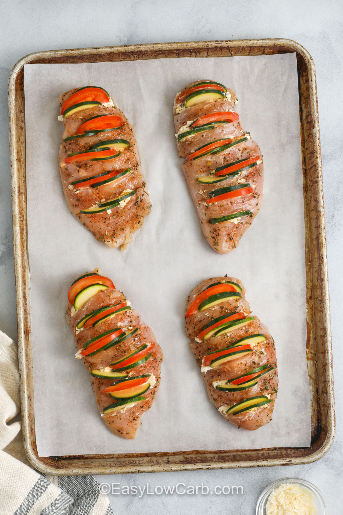 Hasselback chicken transforms plain chicken breasts into a cheesy, veggie-stuffed delight. Each cut is filled with a blend of cream cheese, lemon zest, and tender slices of zucchini and tomato. It’s low in carbs, high in flavor, and perfect for impressing guests without much effort. This baked dish comes together fast, and the oven does all the hard work for you. Easy, healthy, and delicious! #easylowcarb prepared hasselback chicken on a baking sheet