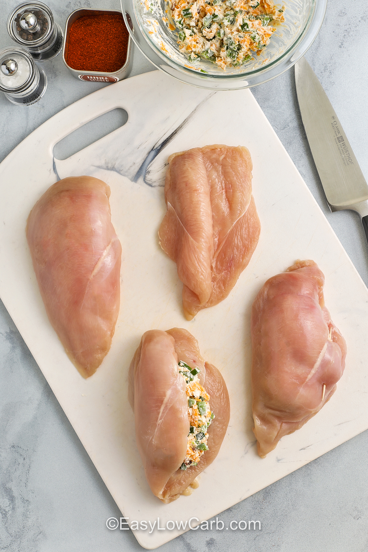 chicken breasts on a cutting board being stuffed with the filling to make jalapeno popper chicken