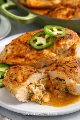 two jalapeno popper chicken breasts on a plate topped with sliced jalapenos with one cut in half and the filling melting out