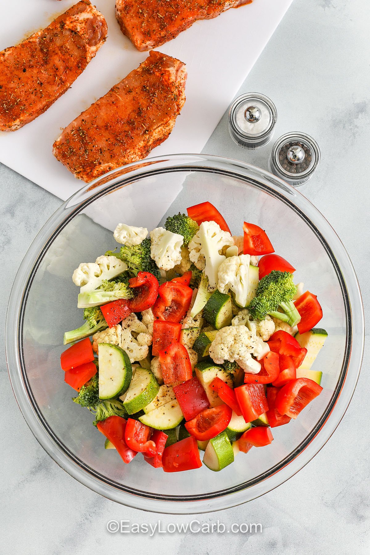 Sheet pan pork chops make dinner stress-free without sacrificing flavor. With just one bowl and one pan, you’ll prep a full meal featuring seasoned pork chops and crispy roasted vegetables. It’s low-carb, gluten-free, and customizable to whatever produce you have on hand. Add mushrooms, asparagus, or even Brussels sprouts to make it your own. #easylowcarb vegetables combined in a bowl while the ork chops marinade