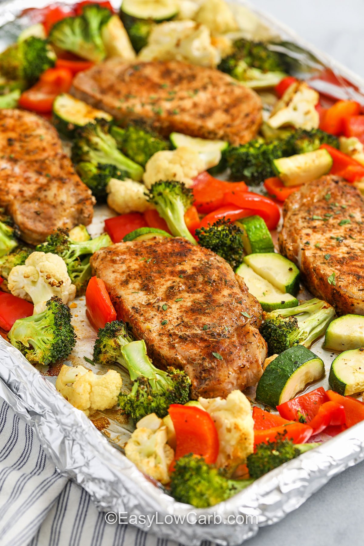 Sheet pan pork chops are your shortcut to a hearty, nutritious dinner with tons of flavor. The spice rub brings smoky, garlicky goodness to the chops, while the oven-roasted vegetables soak up all the tasty drippings. It’s the perfect way to eat more veggies without feeling like you’re missing out. Great for keto, paleo, or clean eating plans. #easylowcarb Pork chops and vegetables cooked on baking sheet lined with foil