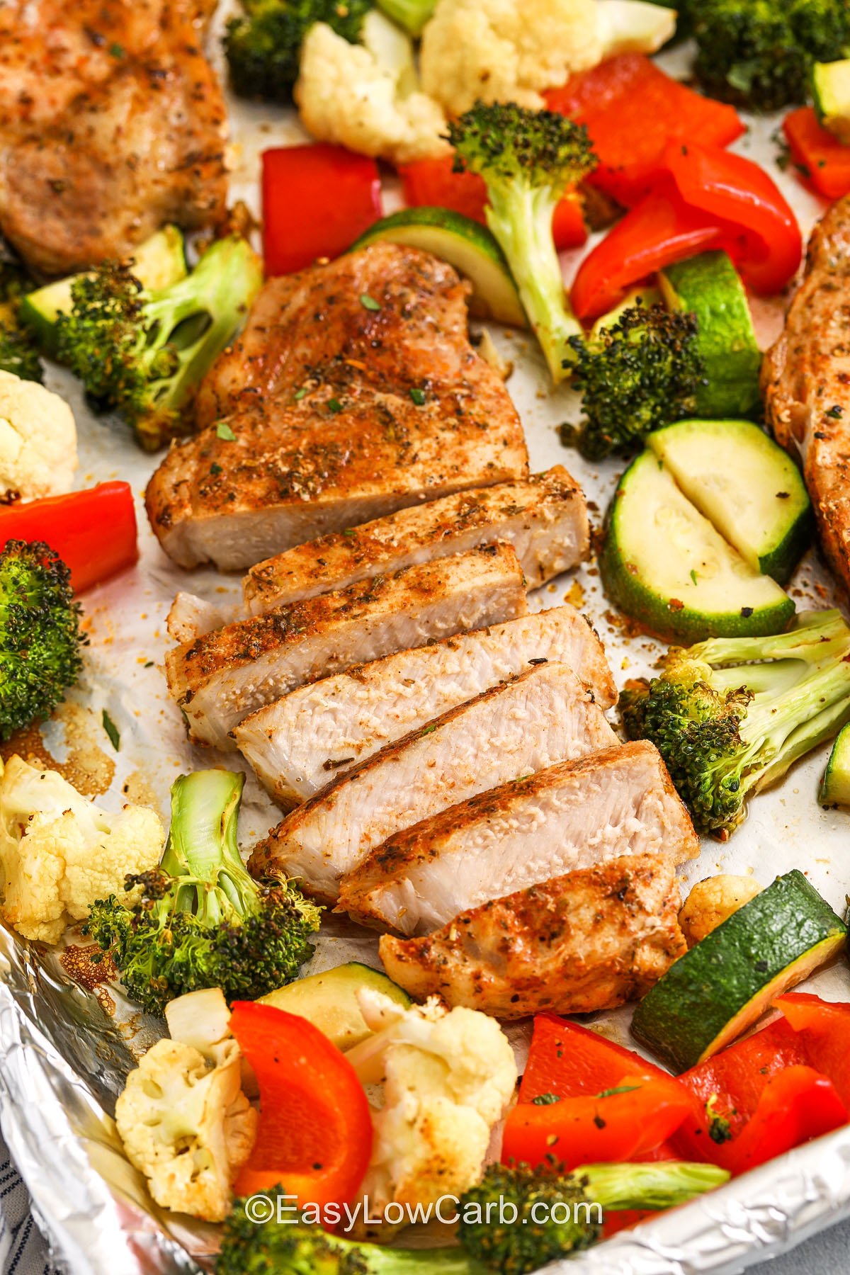 Sheet pan pork chops with roasted vegetables are a flavor-packed, low-carb dinner that’s ready fast. Seasoned with Italian herbs, garlic, and paprika, the pork bakes up perfectly while the veggies become tender and slightly crispy. It’s a complete meal in one pan with zero need for side dishes or extra cleanup. Weeknight dinner solved. #easylowcarb a cooked pork chop sliced on a baking sheet with vegetables