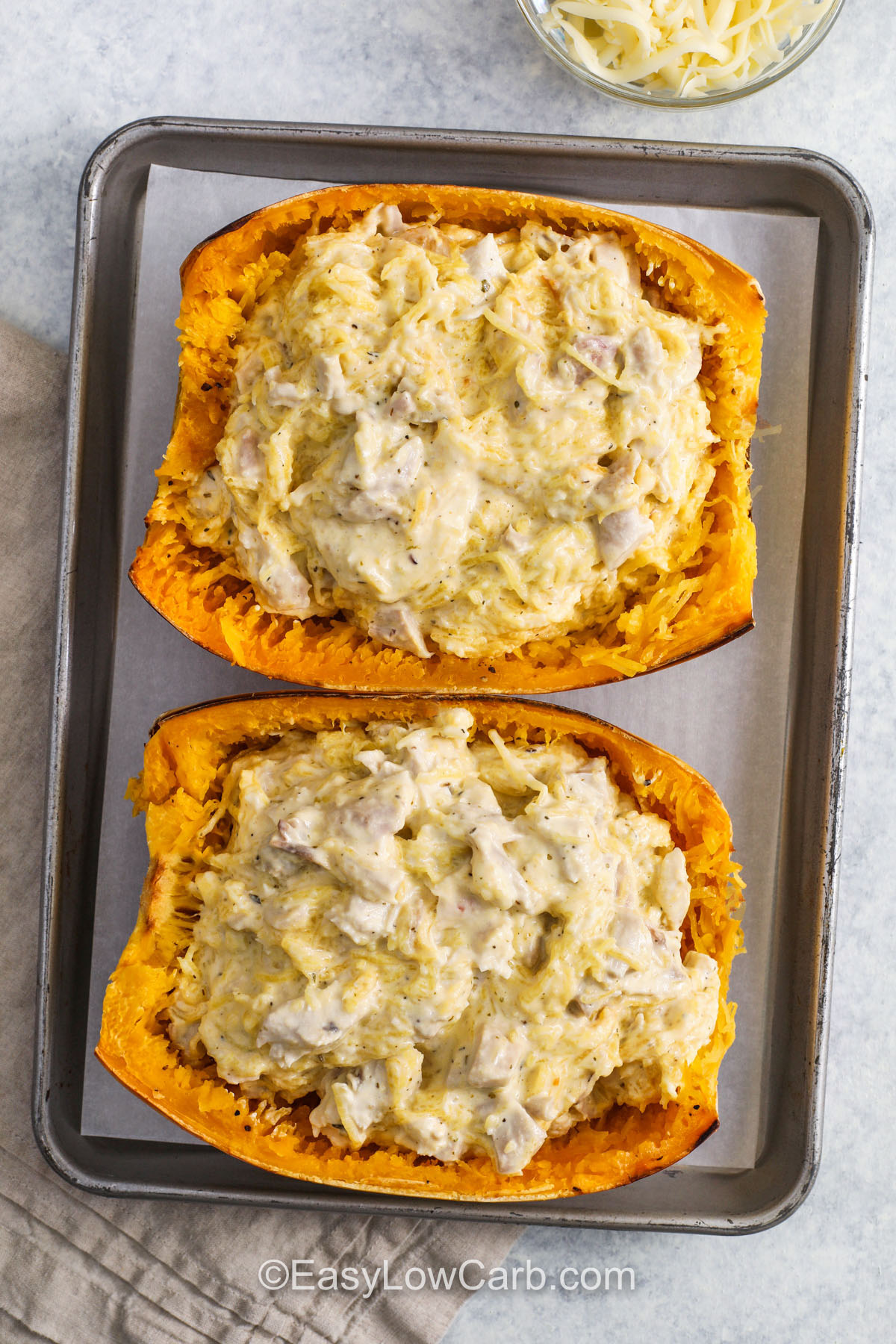 Spaghetti squash chicken Alfredo transforms a beloved pasta dish into a guilt-free pleasure. The squash bakes to tender perfection, creating natural noodles that pair beautifully with the creamy Alfredo sauce. Infused with garlic, butter, and Parmesan, and loaded with chicken and melted cheese, it’s a restaurant-worthy dinner you can make easily at home any night. #easylowcarb Spaghetti Squash Chicken Alfredo on a sheet pan before cooking