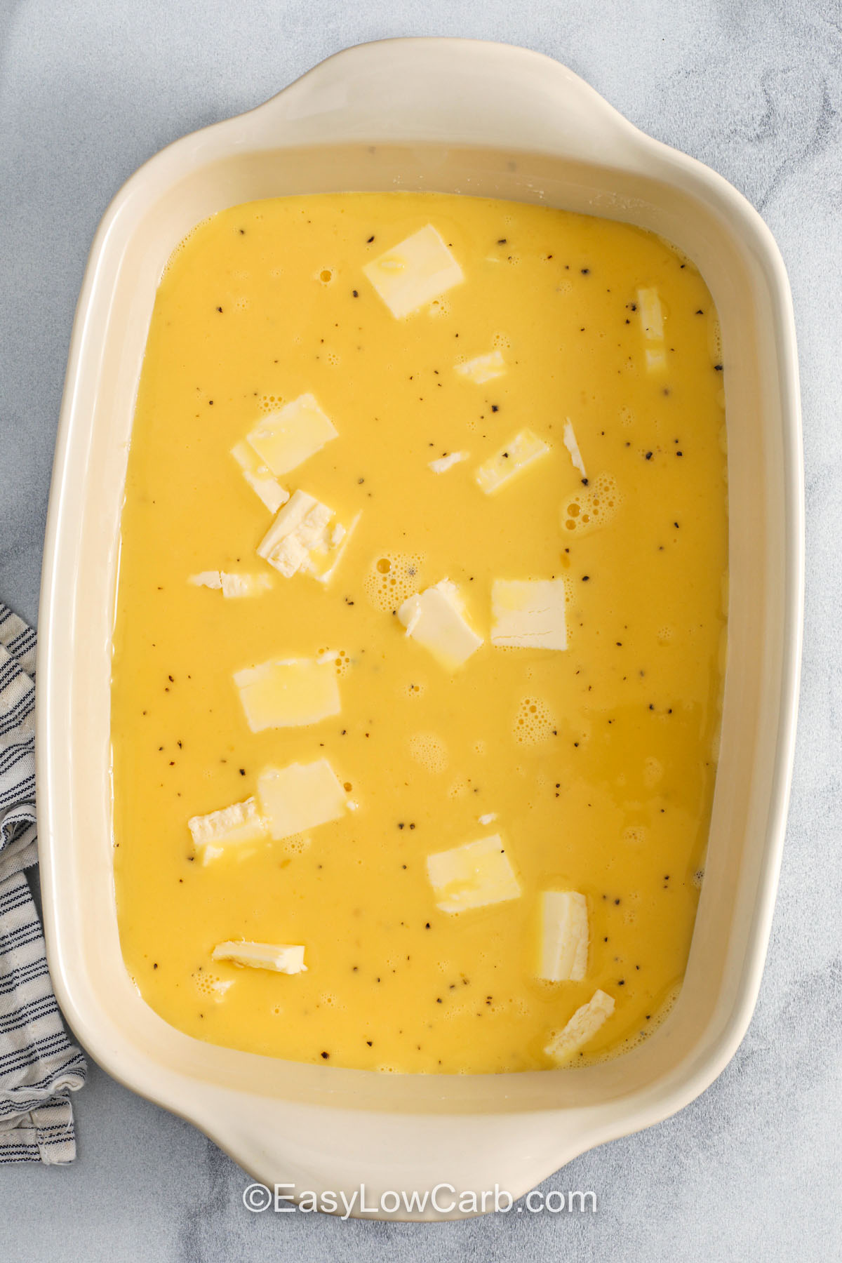 Baked scrambled eggs bring a steady and fluffy breakfast dish that uses the oven to bake everything evenly. This easy sheet pan recipe feeds a crowd and invites simple add-ins like cheese or herbs to suit your taste. It works well as a make-ahead meal and is also perfect for brunch when you want something warm and simple to share. Serve it with fruit or greens for a full plate. #easylowcarb adding ingredients to casserole dish to make Baked Scrambled Eggs