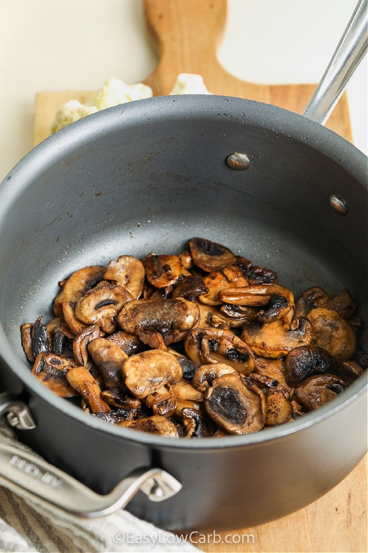 You’ll love this recipe for cauliflower mushroom soup. This low-carb version uses cauliflower for a naturally creamy texture. It’s quick to prepare with just a few pantry staples like garlic, broth, and thyme. The mushrooms bring depth, while cream cheese gives a rich finish. Blend until silky smooth and serve with a swirl of cream and sautéed mushrooms on top. Low-carb comfort food at its best. #easylowcarb adding mushrooms to the pot to make recipe for Cauliflower Mushroom Soup