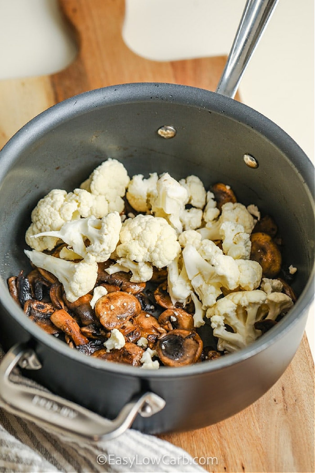 This recipe for cauliflower mushroom soup doesn’t need carbs to be creamy and flavorful. With fresh mushrooms, garlic, chicken broth, and cauliflower, this soup blends into a deliciously smooth and hearty meal. A little cream cheese adds richness without heaviness. Ideal for meal prep or a cozy weeknight dinner. Garnish with reserved mushrooms and optional cream for a restaurant-style touch. #easylowcarb adding cauliflower to pot to make Cauliflower Mushroom Soup