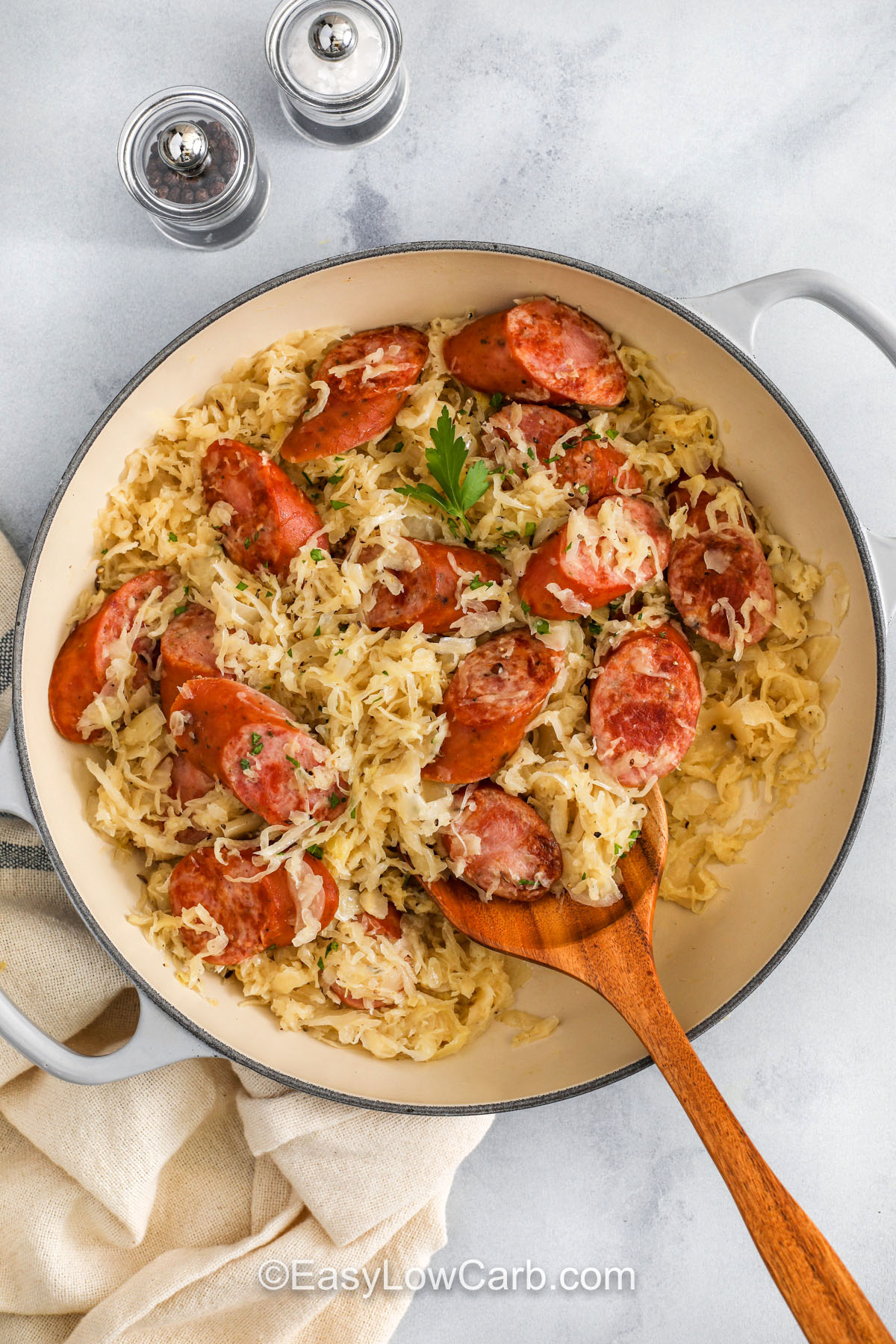 Kielbasa and sauerkraut brings rich flavor to a skillet with browned sausage, tender cabbage, and a savory mix of broth and mustard that turns into a hearty dinner made for everyday cooking. This easy recipe works well as a one-pot meal and adds comfort to the table for a weeknight or a holiday. Serve it on its own or with warm sides to make each bite feel like the best kind of simple home-style meal. #easylowcarb pan of Kielbasa and Sauerkraut with wooden spoon