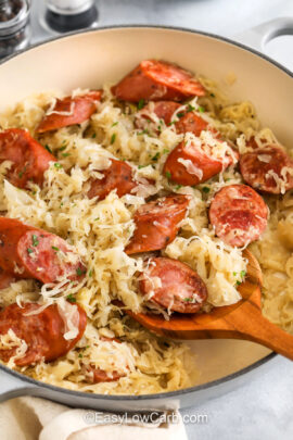 close up of Kielbasa and Sauerkraut in a pan with a wooden spoon
