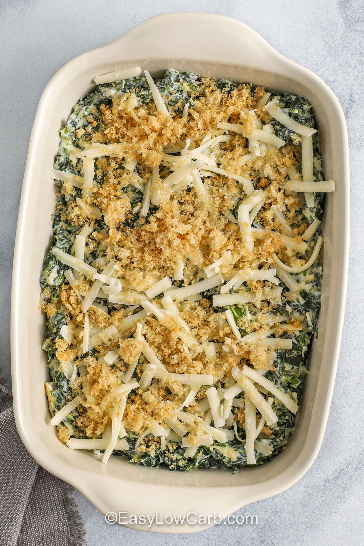 Spinach casserole blends creamed spinach with cream and cheese for a simple baked side that turns soft and warm. The flavor feels old-fashioned and comforting, and works well for dinner with family or a holiday crowd. It is a great potluck choice and adds a rich, cheesy taste to the meal. This recipe has a creamy and cheesy flavor in every bite and pairs well with many mains. #easylowcarb adding ingredients to casserole dish to make Spinach Casserole