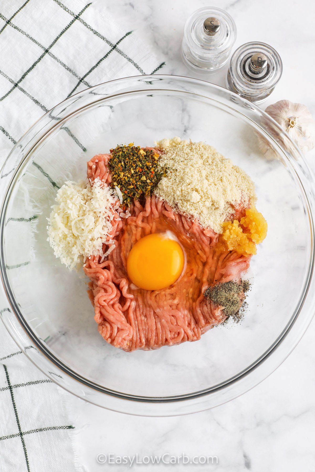 Make a batch of low carb baked chicken meatballs with simple ingredients like ground chicken, egg, parmesan cheese, and Italian seasoning. Almond flour keeps them gluten free while still giving that familiar meatball texture. Bake them in the oven until cooked through, then spoon over your favorite low sugar marinara or pesto. These chicken meatballs are perfect for meal prep, lunch bowls, and family dinners that feel comforting. #easylowcarb adding ingredients to bowl to make Chicken Meatballs