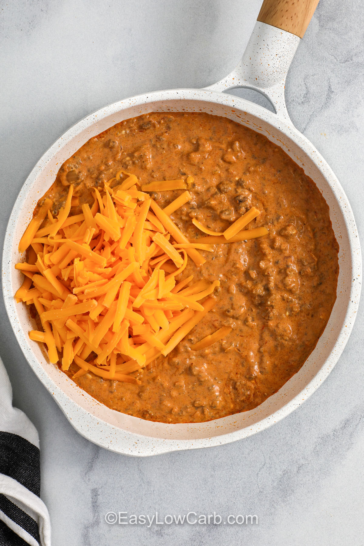 Make a beefy queso-style Chili Cheese Dip that comes together easily. Cook ground beef, drain, and season it, and then stir in salsa and cream cheese until smooth and creamy. Finish with sharp cheddar for a bold, cheesy bite. This low carb dip is great with crunchy veggie dippers and can be kept warm for serving. For best results, use block cheddar you shred yourself and keep the heat low once dairy is added. #easylowcarb adding cheese to pan to make Chili Cheese Dip