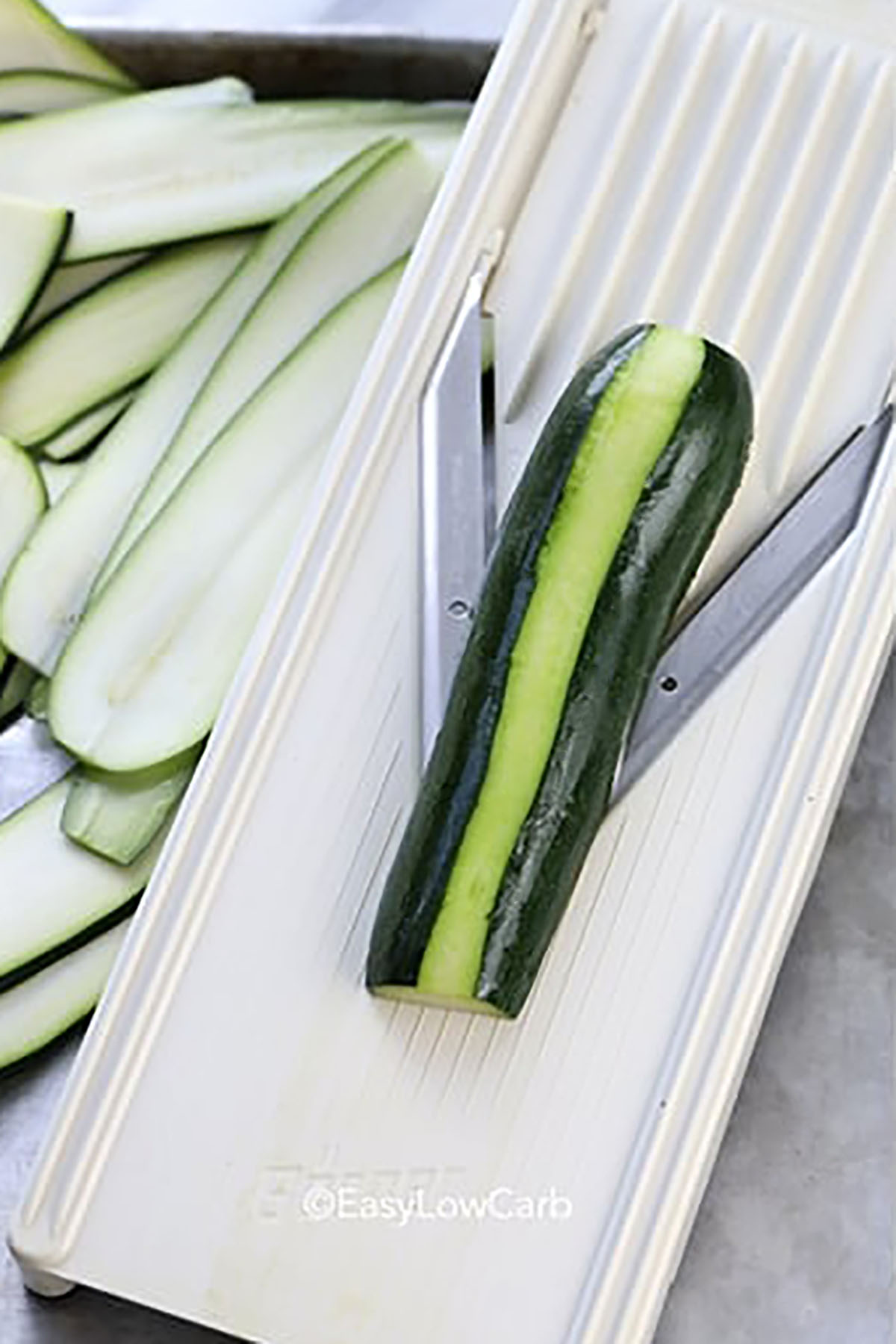 Enjoy hearty Tex-Mex flavor without the carbs from tortillas, with these keto zucchini enchiladas. Fresh zucchini is sliced into long strips, then wrapped around a warm chicken and enchilada sauce filling. A blend of sharp cheddar and Monterey Jack melts over the top, creating a cheesy crust that covers every roll. This recipe is easy enough for weeknights and works perfectly with leftover or rotisserie chicken to save time. #easylowcarb slicing zucchini to make Zucchini Enchiladas