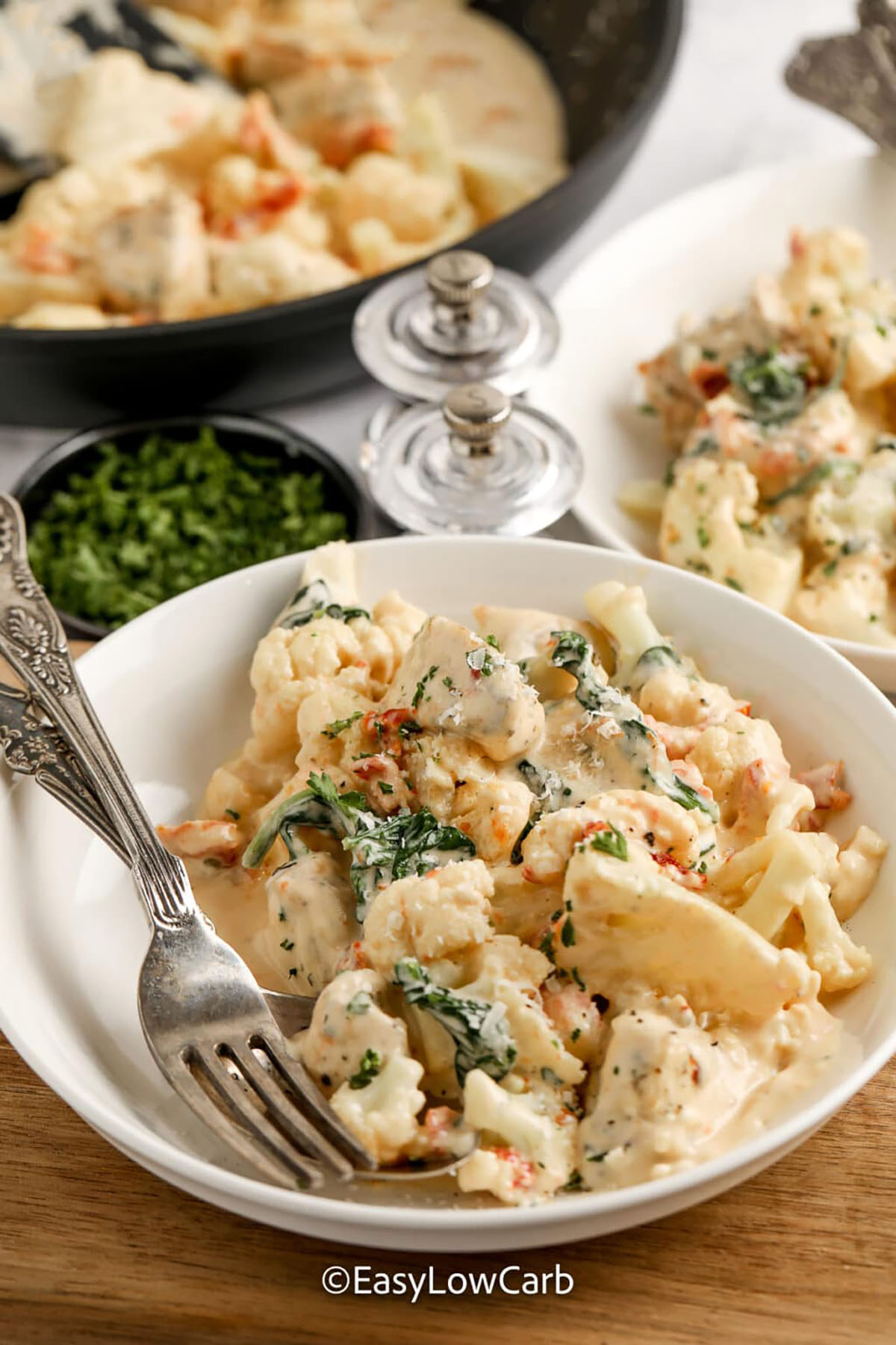 Creamy Tuscan chicken skillet is the low carb dinner that feels special without extra work. Chicken is browned, then finished in a creamy garlic parmesan sauce with oil-packed sun-dried tomatoes and spinach. Cauliflower simmers briefly in broth first, then finishes in the skillet so it stays tender-crisp and the sauce stays thick. Serve as-is or over cauliflower rice for a cozy keto meal. #easylowcarb tuscan chicken in a white bowl with a fork