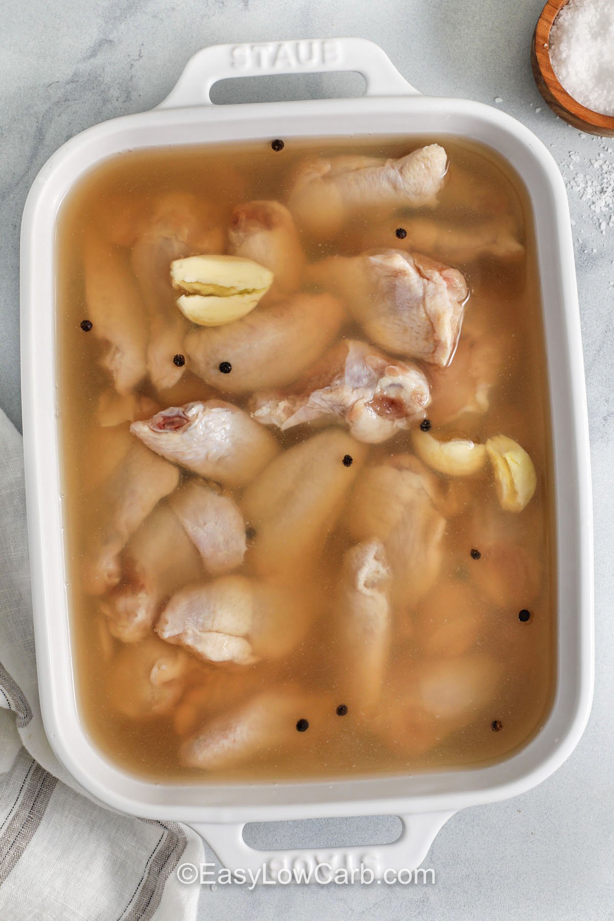 Chicken wing brine is a simple make-ahead step that improves both juiciness and seasoning. Mix water and kosher salt until dissolved, then add Worcestershire, peppercorns, and garlic. Brine wings in a baking dish, then pat dry and cook hot for crisp skin. This low carb method works with classic buffalo, salt and pepper wings, or a smoky dry rub. #easylowcarb Chicken Wing Brine in a dish with chicken wings