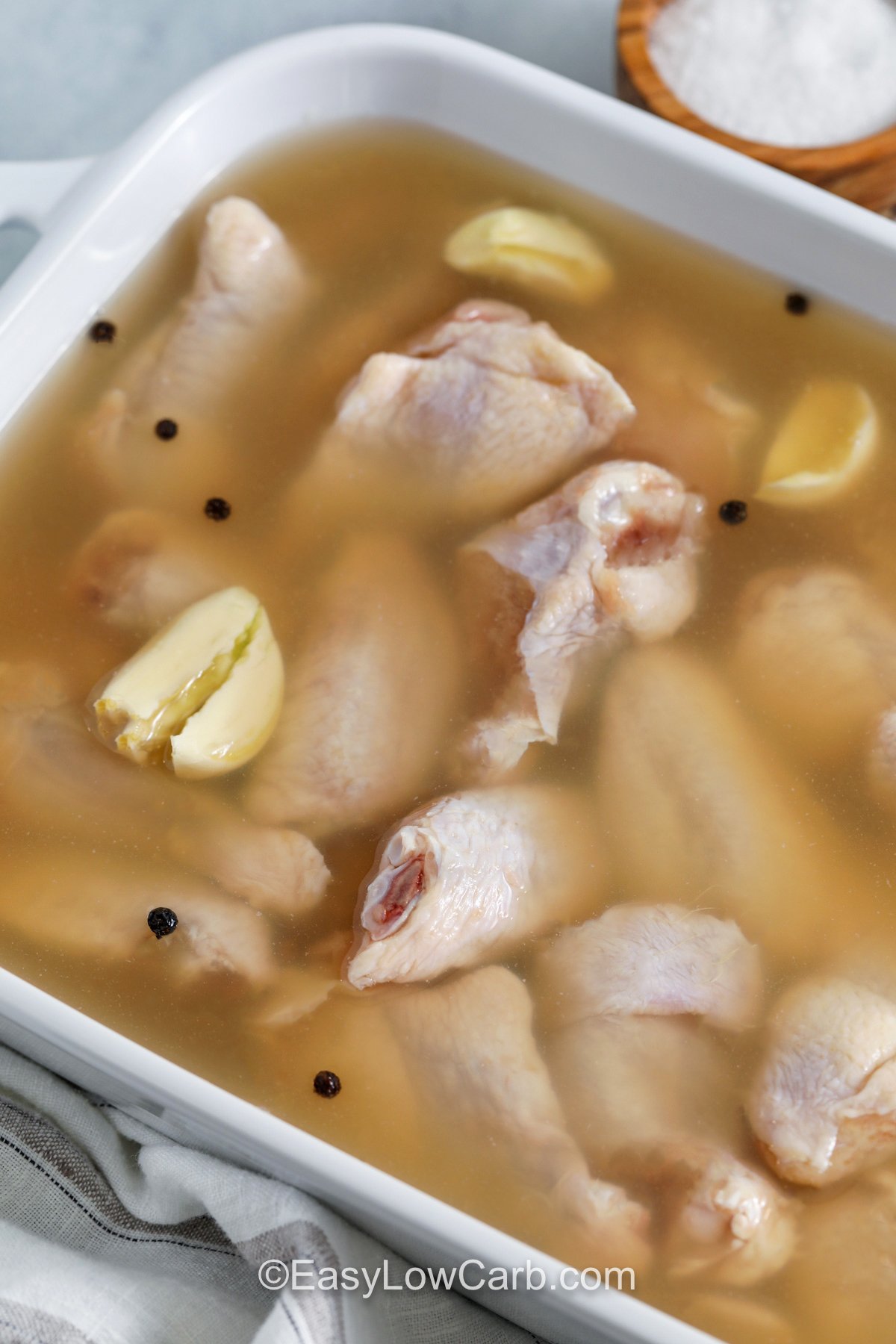 This chicken wing brine combines water, kosher salt, Worcestershire sauce, peppercorns, and smashed garlic to season the wings thoroughly. A short wet brine helps wings stay juicy, especially when baking or air frying. Drain the brine, pat the wings very dry, then cook until crisp and finish with buffalo sauce, garlic parmesan, or your favorite low-carb dry rub. #easylowcarb close up of Chicken Wing Brine with chicken