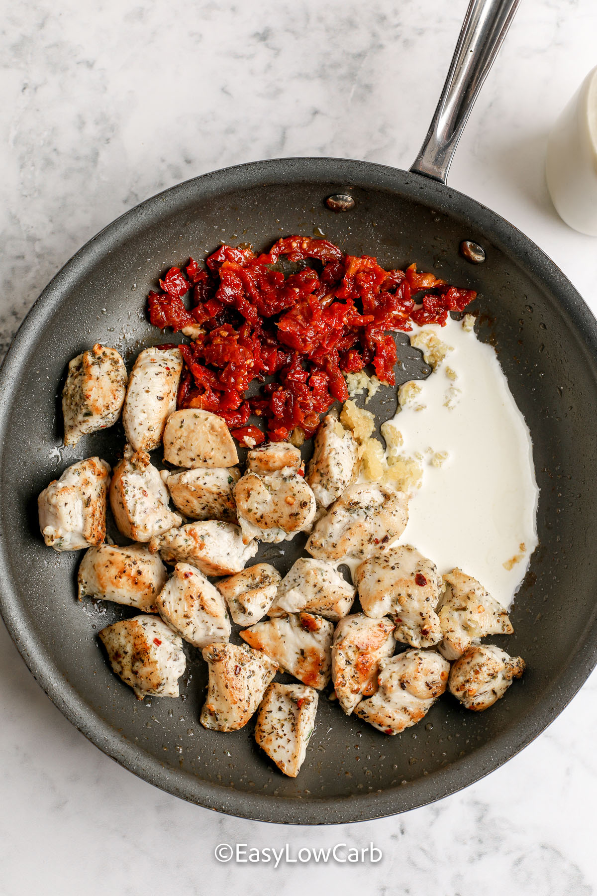 Creamy Tuscan chicken skillet has all the Tuscan flavor you want, with a thick sauce made from broth, heavy cream, and parmesan cheese. Sun-dried tomatoes add sweet tang, and spinach wilts in at the end. Cauliflower cooks first, then finishes in the sauce, so it stays tender-crisp. This low carb Tuscan chicken is great for weeknights and meal prep. #easylowcarb preparing tuscan chicken. a skillet with chicken sun dried tomatoes and cream