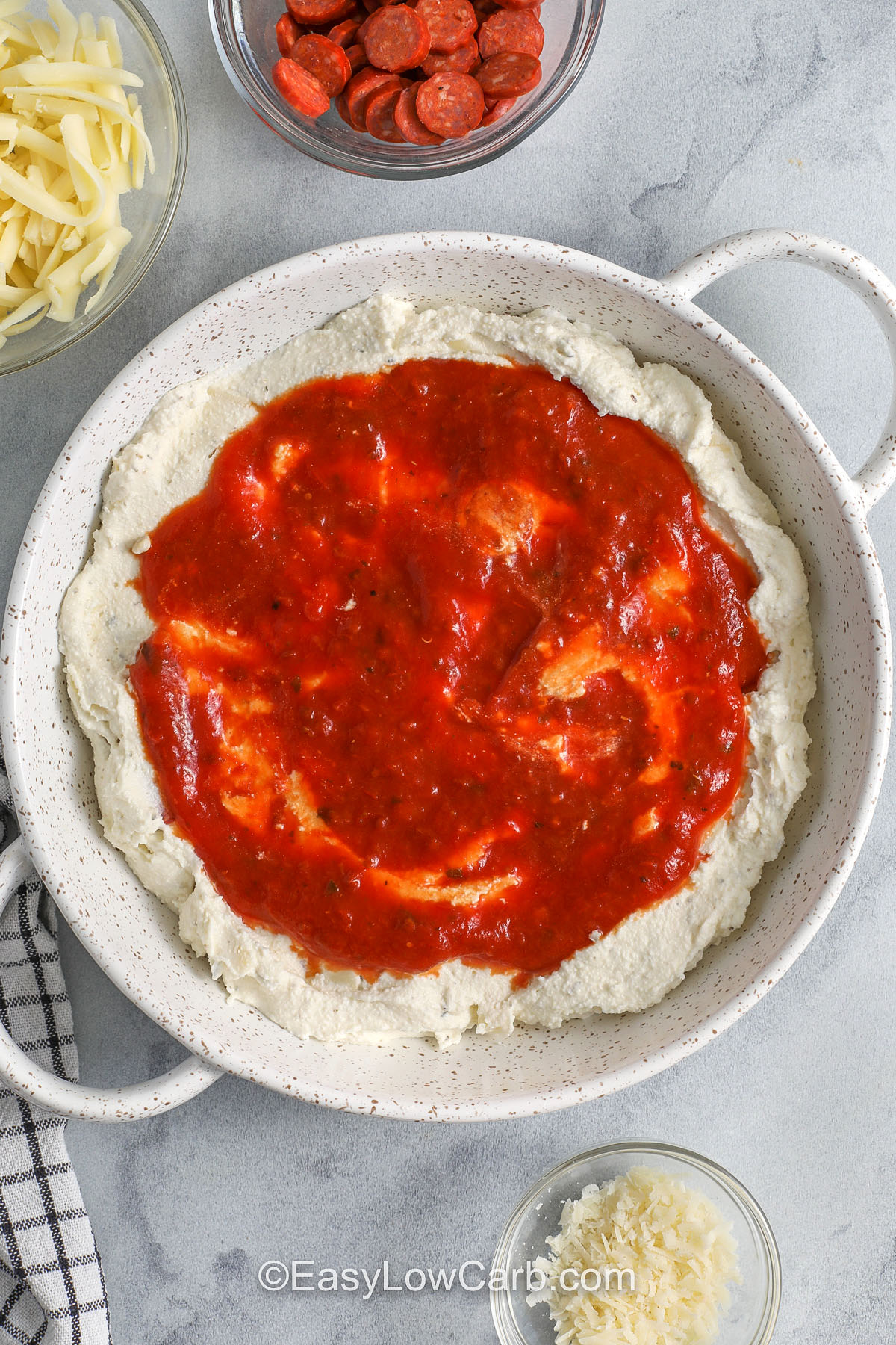 If you love cheesy dips, this pepperoni dip is a must for your snack rotation. Ricotta and cream cheese create a creamy base, while marinara and mozzarella bring classic pizza flavor. Parmesan adds a salty finish, and pepperoni baked on top gives that irresistible savory bite. Serve it hot and bubbly with cucumbers, celery, or pepperoni chips for a low carb option. #easylowcarb adding cheese mixture then marinara layer to dish to make Pepperoni Dip