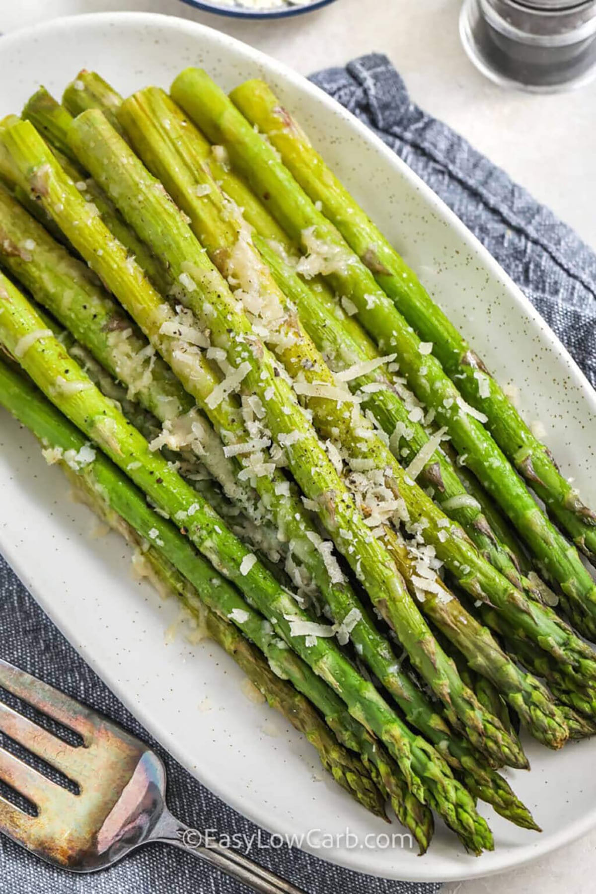 Parmesan asparagus is an easy roasted vegetable side that brings big flavor to the table. Fresh asparagus is tossed with olive oil, garlic, salt, and pepper, then roasted until tender. A layer of grated Parmesan melts on top under the broiler for a golden finish that makes every bite savory and satisfying. Serve this baked asparagus recipe with grilled chicken, steak, or seafood for a simple, low-carb dinner side that always fits into everyday meals. #easylowcarb plated Parmesan Asparagus with with a fork