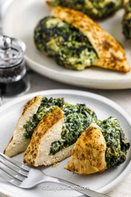 tender Spinach Stuffed Chicken Breasts on a plate and one plated and sliced with a fork beside it