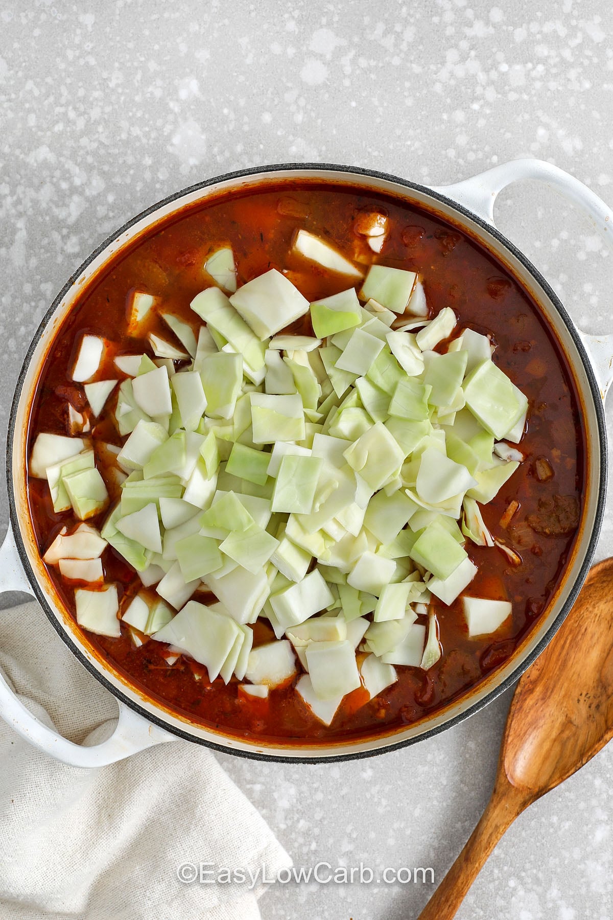 Beef and cabbage soup is a satisfying low carb beef soup that feels like a full meal. The broth is tomato-rich and savory, boosted with Worcestershire and herbs. Brown the beef in batches for the best flavor, then let it simmer until fork-tender. Finish by simmering cabbage until tender. Serve with parmesan or fresh parsley, and enjoy leftovers that taste even better the next day. #easylowcarb adding cabbage to pot to make Beef and Cabbage Soup