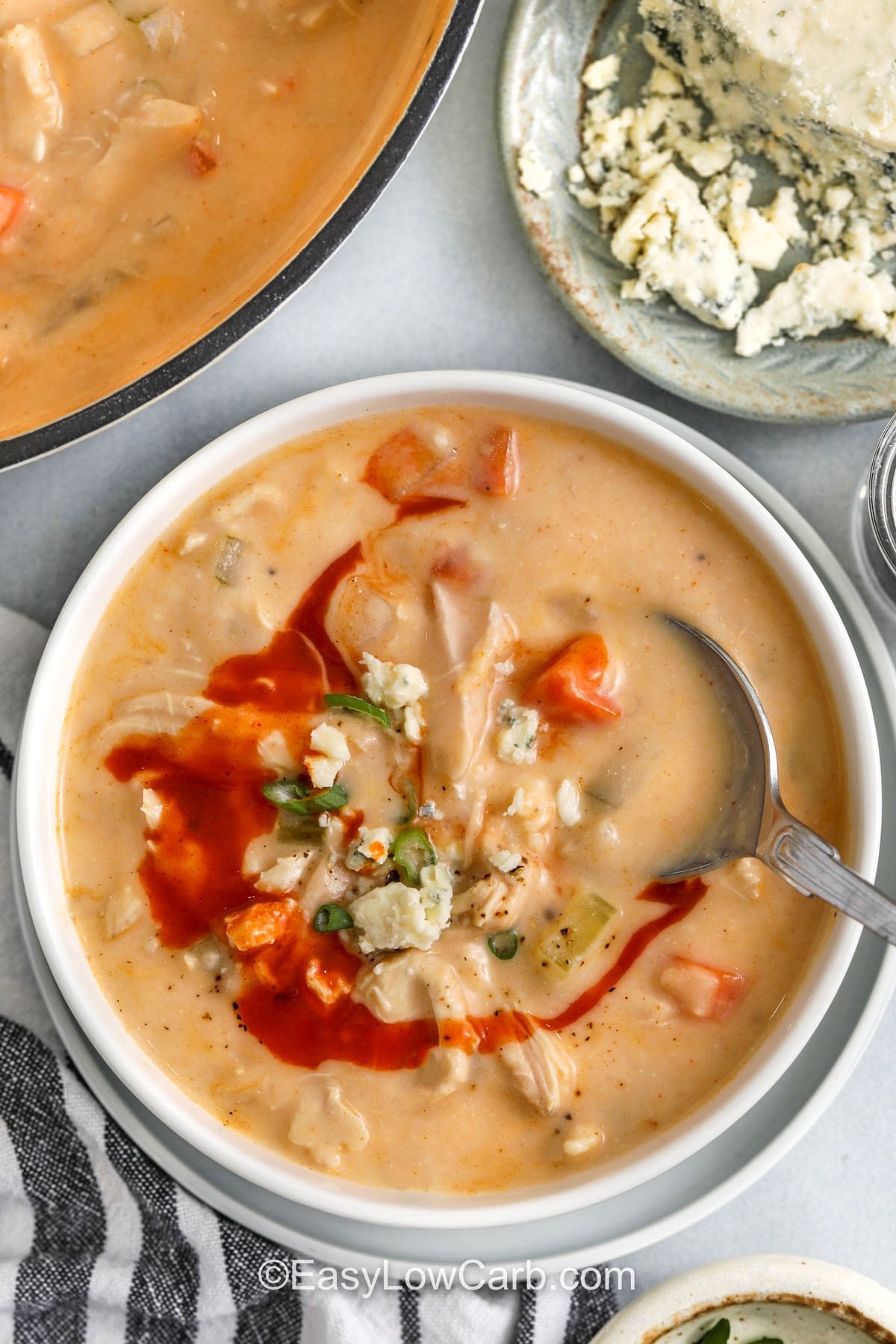 Make creamy buffalo chicken soup when you want big flavor with everyday ingredients. A quick boil and blend turns cauliflower into a silky puree that gives the soup body. Cream cheese adds richness, celery brings classic wing flavor, and shredded chicken makes it satisfying. Add buffalo sauce slowly to control heat, then top with cheddar or blue cheese and fresh green onions. #easylowcarb bowl of Buffalo Chicken Soup with a spoon
