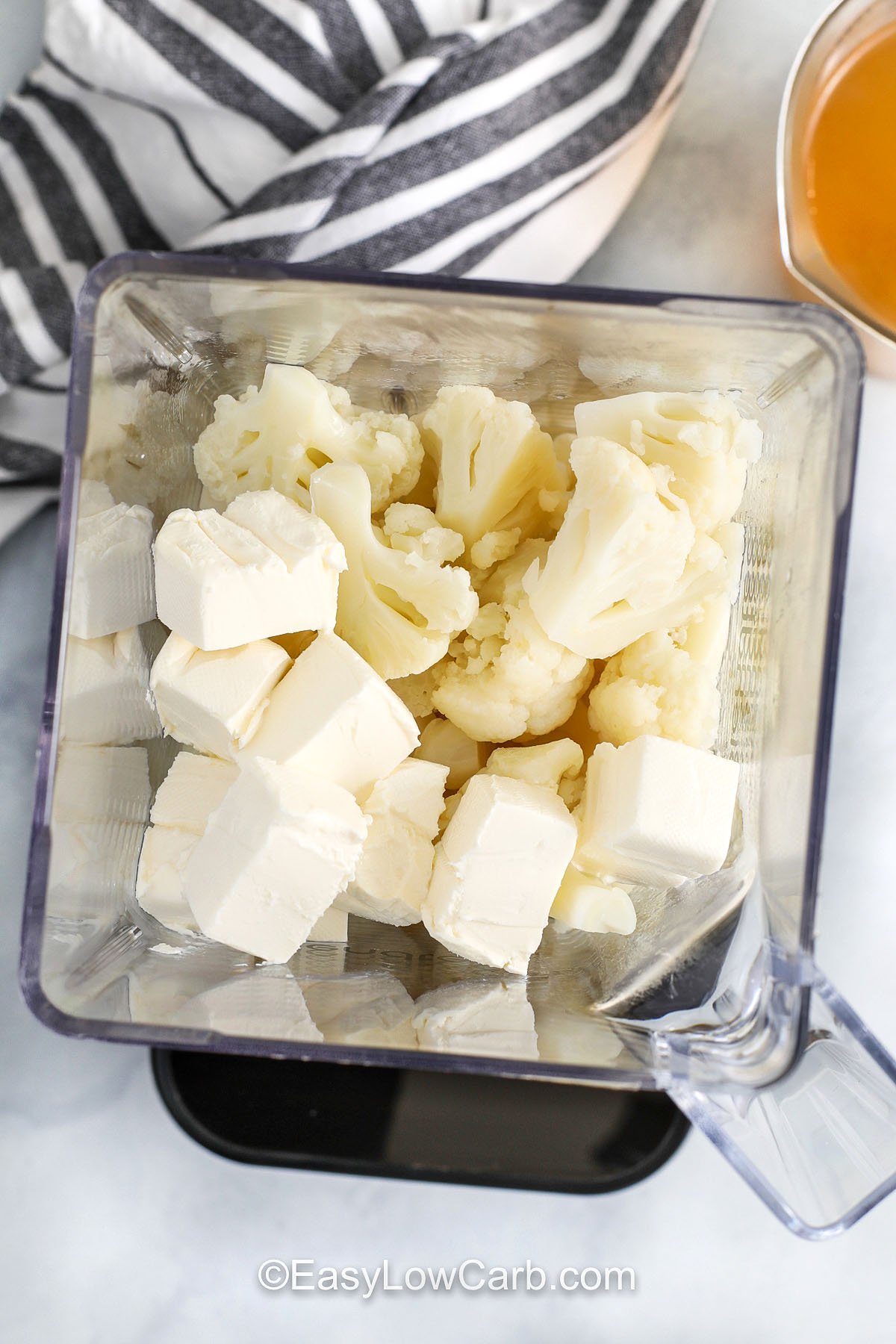 Creamy buffalo chicken soup is an easy low carb dinner that tastes like buffalo chicken dip in soup form. Boiled cauliflower blends silky with cream cheese, creating a thick base that clings to every bite. Simmer it with celery and onion for that wing-night vibe, then add shredded chicken and buffalo sauce just to heat through. Finish with blue cheese crumbles and sliced green onions. #easylowcarb adding cream cheese and cauliflower to blender to make Buffalo Chicken Soup