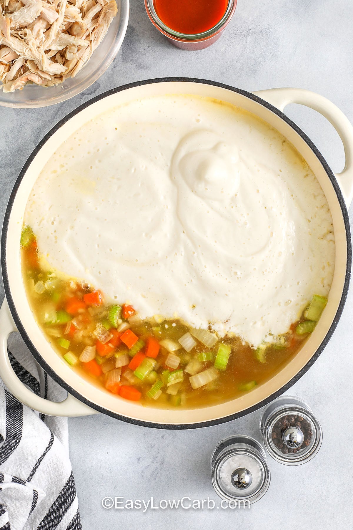 If you love spicy comfort food, buffalo chicken soup is a weeknight win. The cauliflower puree makes the soup thick and velvety, and it keeps the recipe low carb without extra thickeners. Shredded chicken turns it into a filling meal, and buffalo sauce brings the tangy kick. Serve with cheddar or blue cheese and a handful of green onions for a bright, savory topping. #easylowcarb adding blended ingredients to broth and vegetables in pot to make Buffalo Chicken Soup