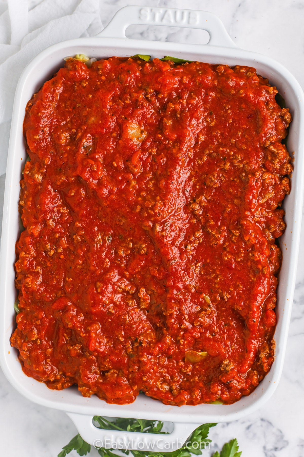 Cabbage Lasagna is a low-carb comfort food dish that delivers the saucy, cheesy layers everyone loves. Boiled cabbage leaves replace noodles and bake up tender and flavorful, pairing well with the meat sauce. A creamy cottage cheese filling sets as it bakes for cheesy goodness. Finish with mozzarella for a bubbly top, then rest before cutting for the best texture and easy serving. #easylowcarb adding meat sauce layer to casserole dish to make Cabbage Lasagna Recipe