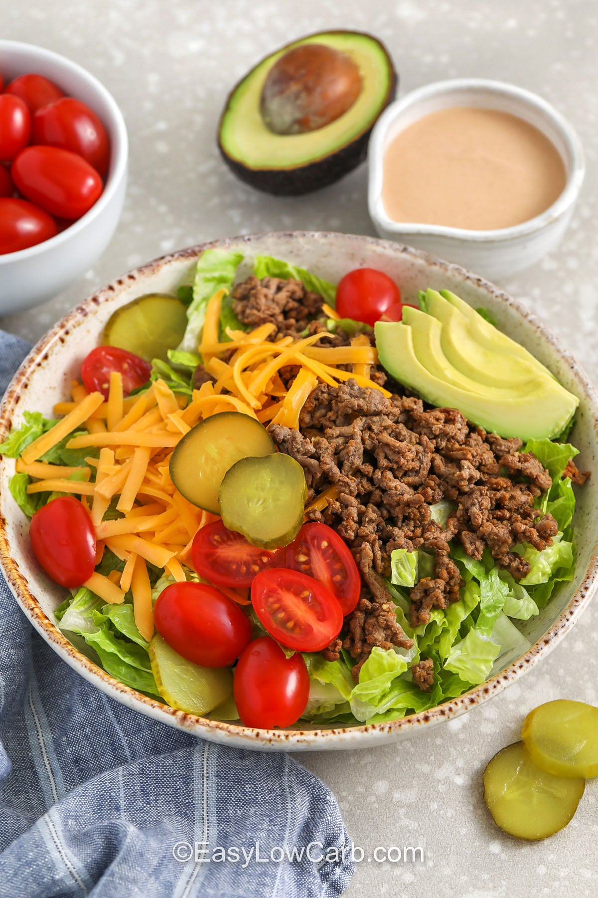 If you love burger night, try a cheeseburger bowl that keeps it low carb and satisfying. Warm smoky ground beef goes over cold crunchy lettuce with cheddar cheese, pickles, tomatoes, and optional bacon bits. The creamy dressing tastes like classic burger sauce and takes minutes to whisk together. Add avocado for extra creaminess, or skip it and keep the bowl lighter while still full of flavor. #easylowcarb plated Cheeseburger Bowl with dressing on the side