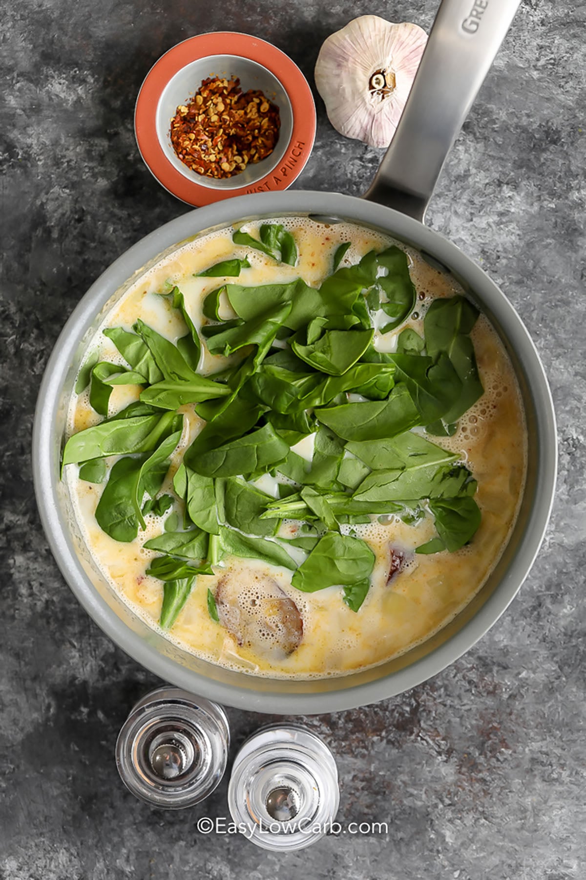 adding liquids and spinach to pan to make Creamy Italian Sausage Soup