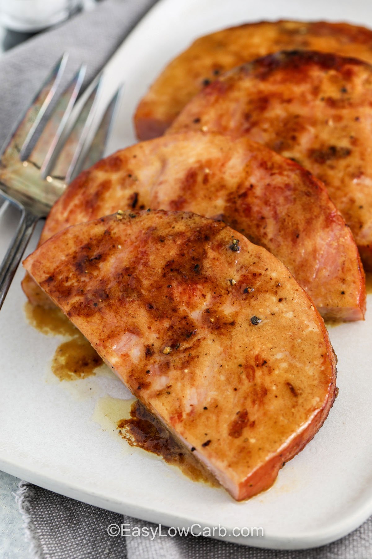 This ham steak recipe is the easiest way to get a cozy dinner on the table fast. Ham steaks sear in butter for light browning, then a Dijon mustard glaze with low carb brown sugar sweetener and apple cider vinegar melts on top. The result is sweet, salty, and tangy with a rich pan sauce you can spoon over every slice. Serve with cauliflower mash or green beans for a simple low carb plate. #easylowcarb close up of Ham Steak on plate