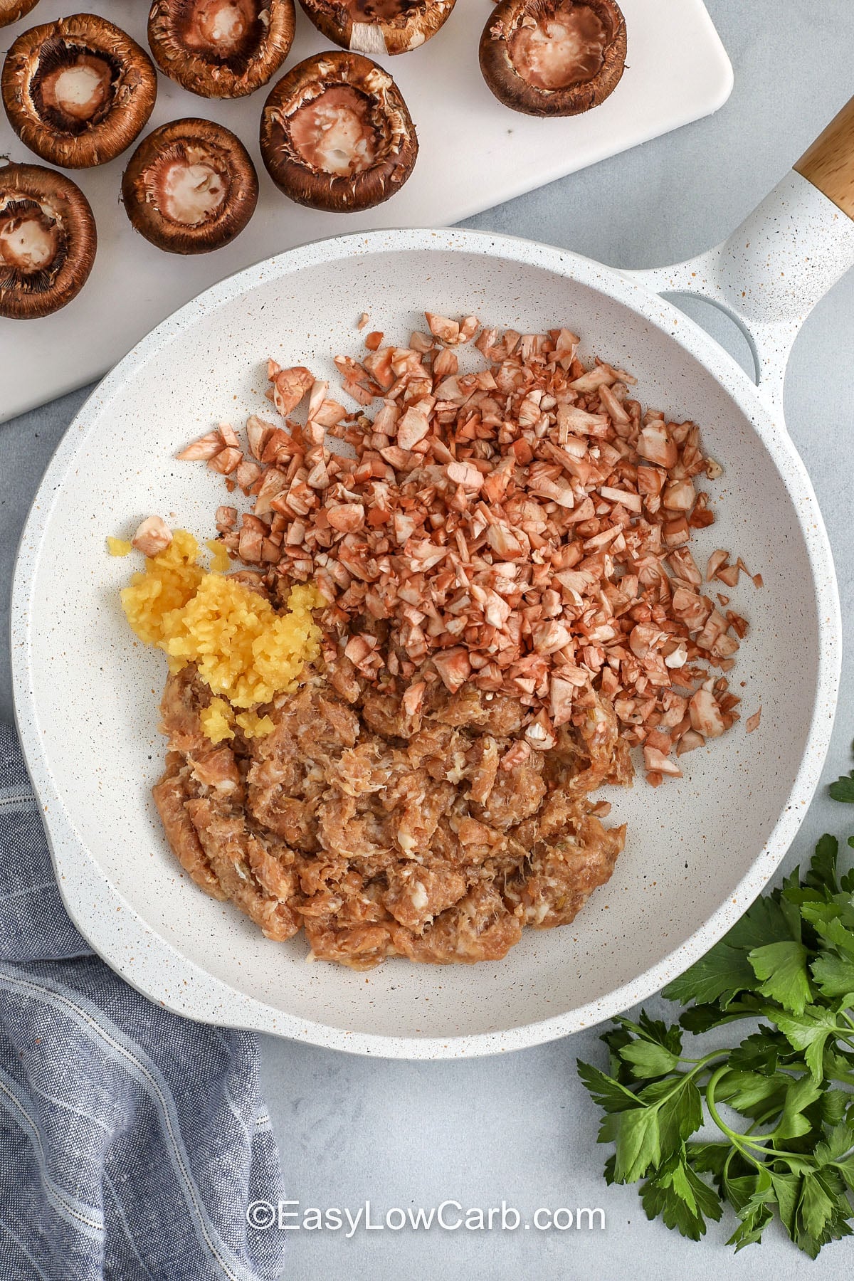 adding sausage , mushroom stems and garlic to pan to make Keto Stuffed Mushrooms