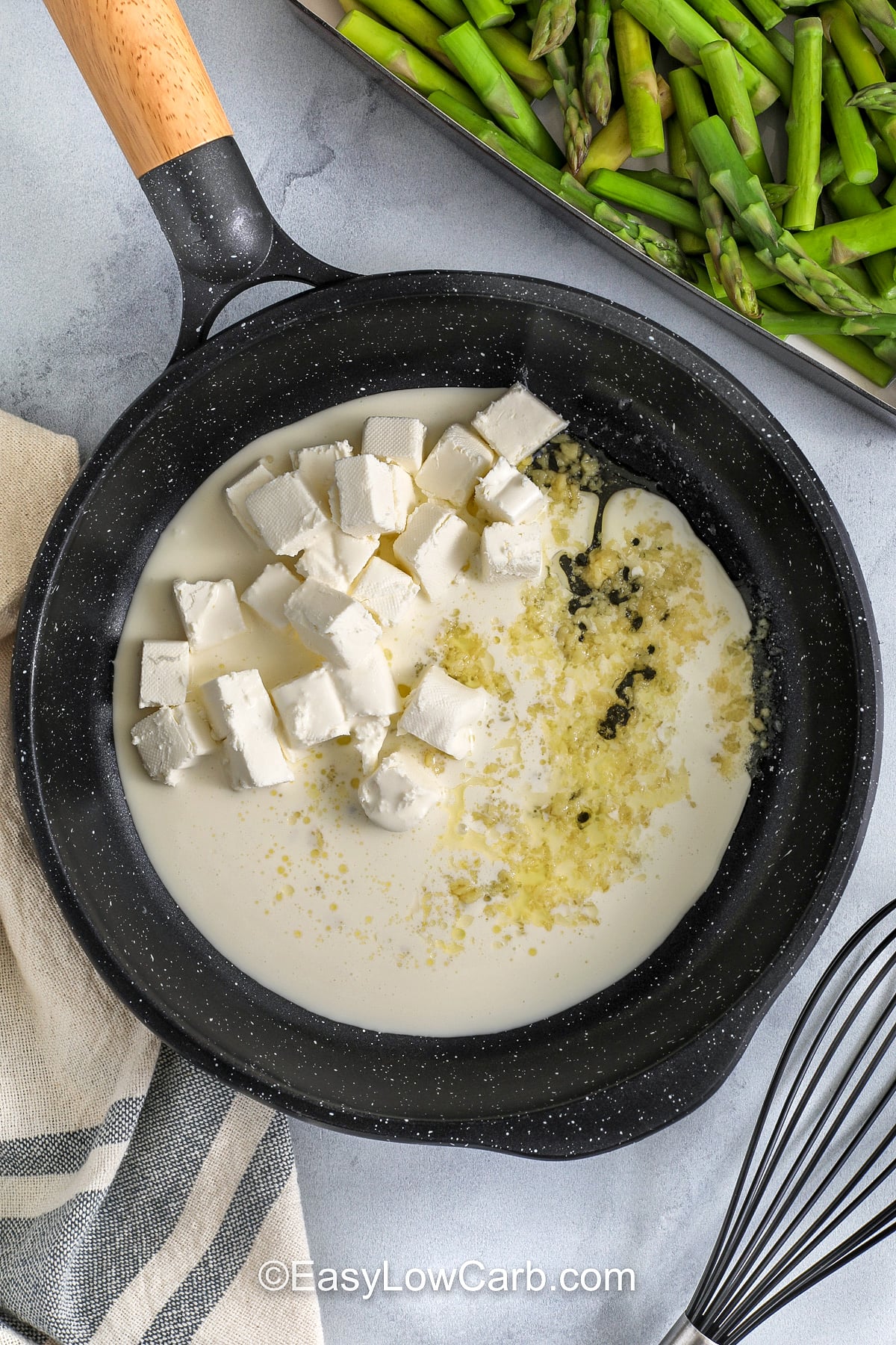 Bake a low carb asparagus casserole for a weeknight side that tastes like a steakhouse favorite. The asparagus stays tender-crisp thanks to a quick blanch, then gets coated in a creamy cheese sauce made with heavy cream, cream cheese, cheddar or gruyere, and parmesan. A crunchy pork rind topping browns beautifully in the oven. Serve with pork chops or roasted chicken for an easy keto dinner. #easylowcarb adding garlic , cream and cream cheese to pan to make sauce for Asparagus Casserole