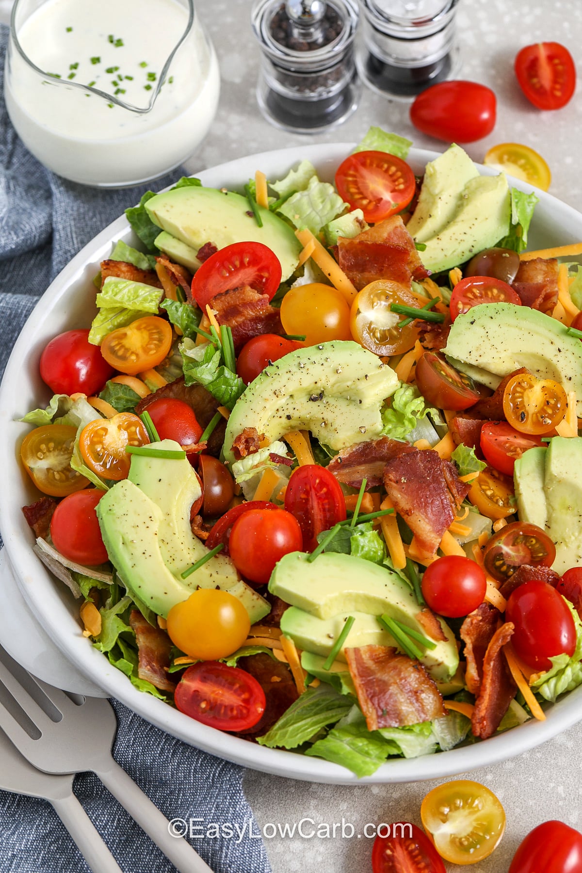 This low carb BLT salad comes together with everyday ingredients and big flavor. Juicy cherry tomatoes, crisp greens, and crumbled bacon are finished with shredded cheddar and sliced avocado. The creamy BLT salad dressing is easy to adjust with a splash of milk so it turns silky and drizzle-friendly. It is perfect for busy weeknights, packed lunches, and simple summer meals. #easylowcarb BLT salad in a white bowl with utensils