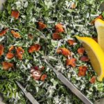 Kale Caesar Salad prepared in a bowl with lemon wedges and serving utensils